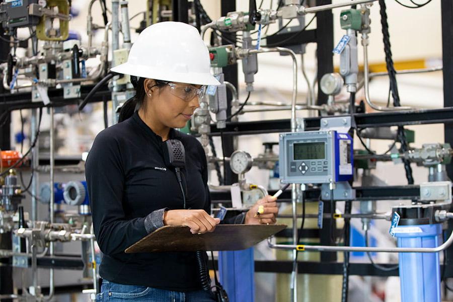 A person in a white hard hat looks at a monitor with various machines in the background